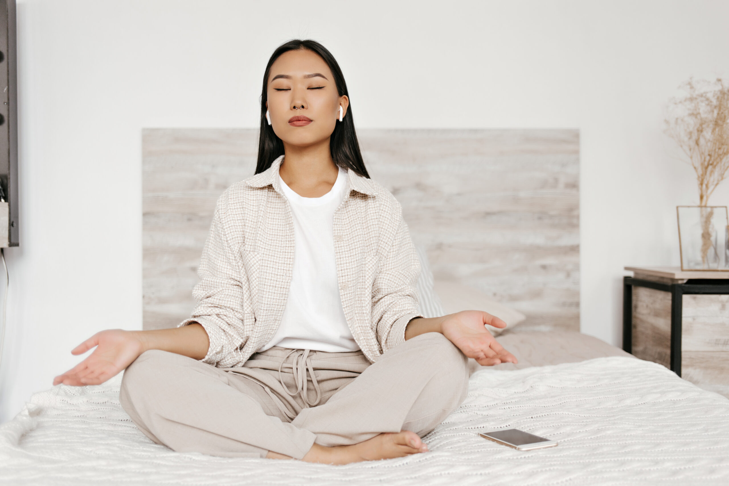 Kobieta medytująca na łóżku w słuchawkach